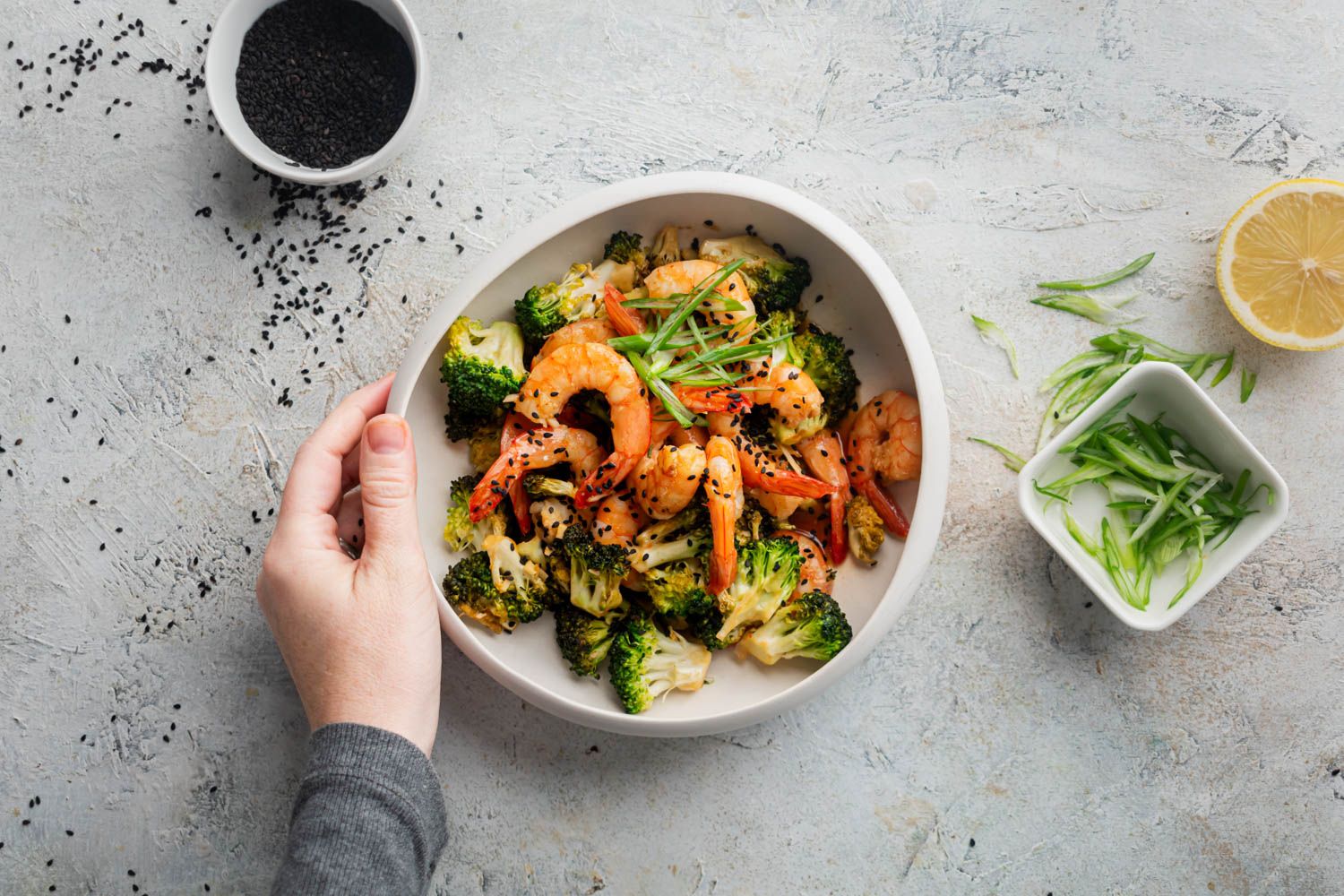 Spicy firecracker shrimp with broccoli florets in a bowl with a hand holding the bowl.