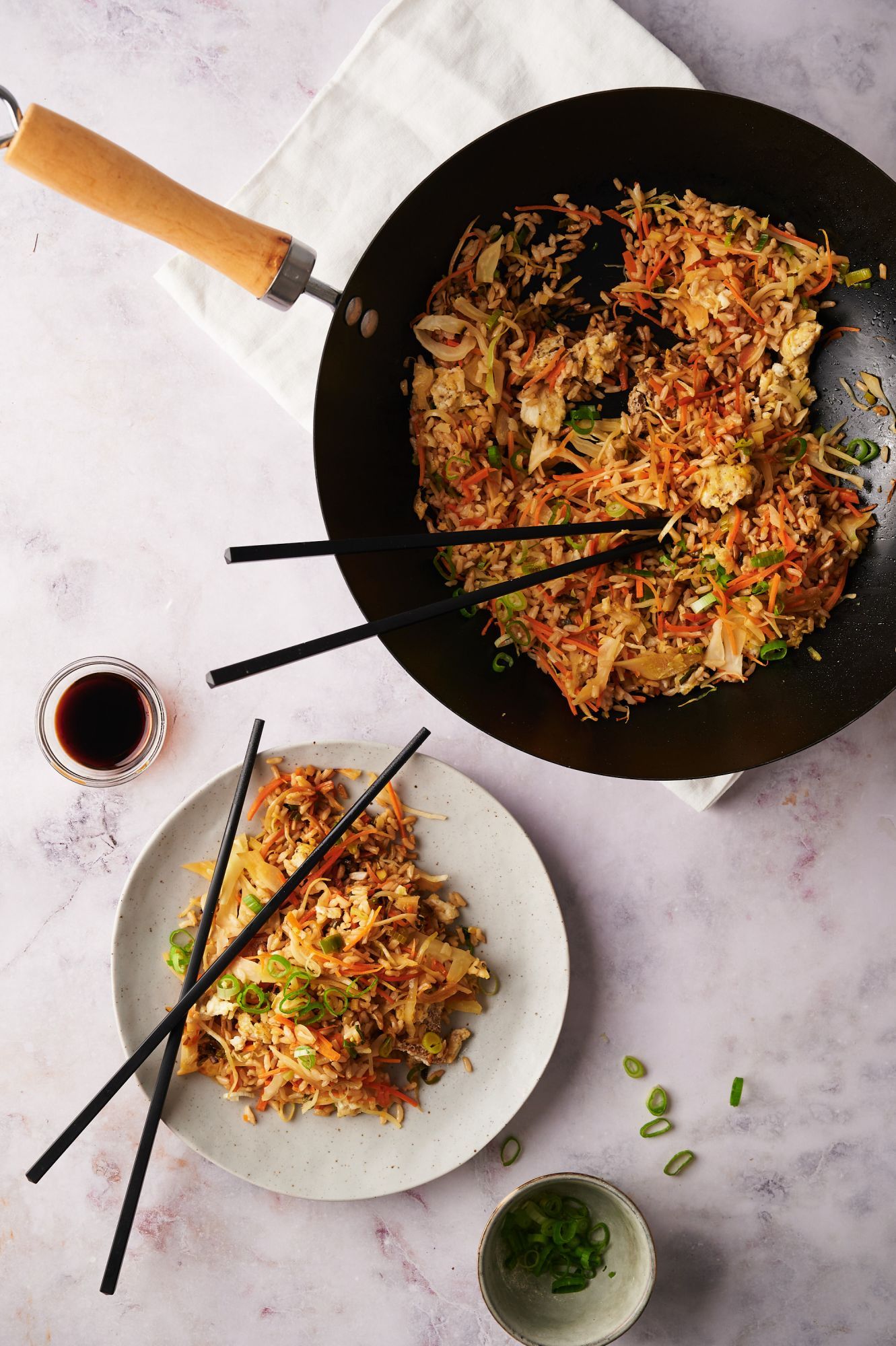 Healthy Asian fried rice with carrots, cabbage, green onions, eggs, and brown rice in a wok and served on a plate.