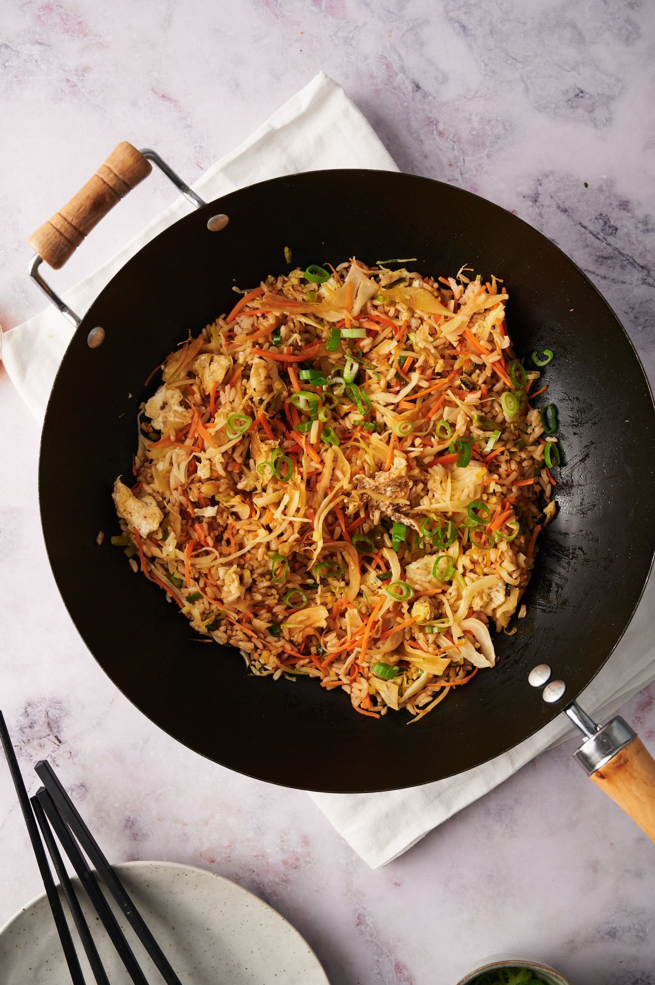 Wok with healthy fried rice made with eggs, carrots, cabbage, sot sauce, and green onions.