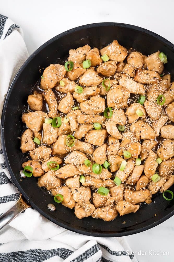 Baked Sesame chicken with sesame seeds and green onions in a skillet.