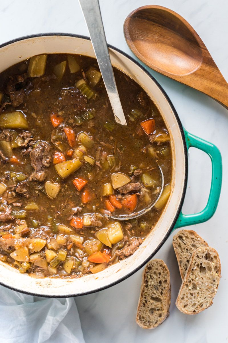 Hearty beef stew with potatoes and carrots in a rich beef broth with onions in a large Dutch oven with a wooden spoon.
