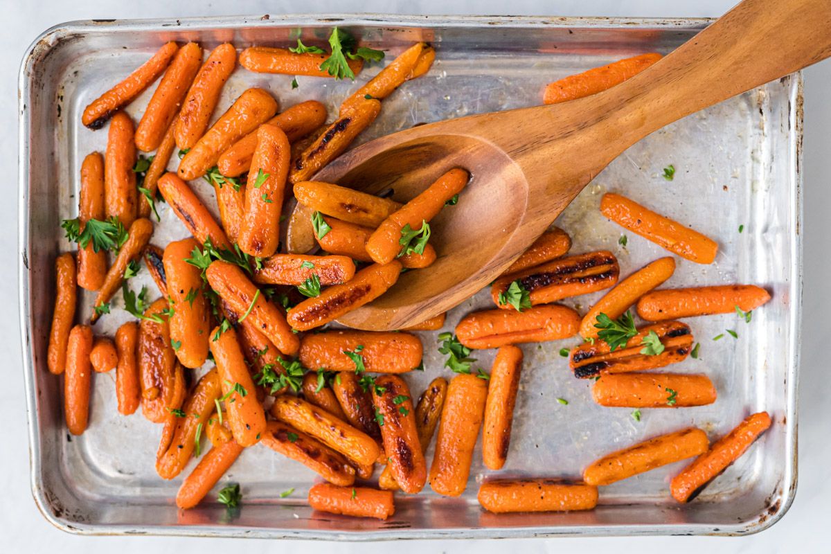Baby carrots roasted on a baking sheet with olive oil, salt, pepper, honey, and parsley.