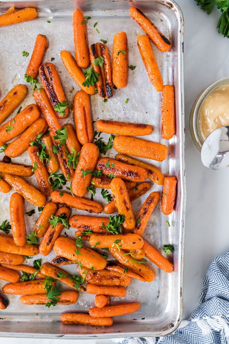 Baby carrots that have been roasted with olive oil and honey on a baking sheet.