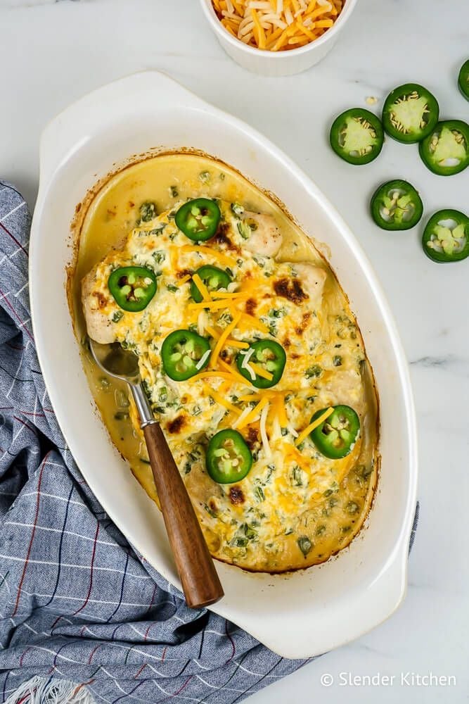 Jalapeno Popper Chicken in a baking dish with fresh jalapenos and cheddar cheese on top.