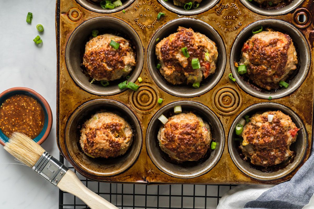 Barbecue turkey meatloaf muffins in a muffin tin with green onions and barbecue sauce on the side.