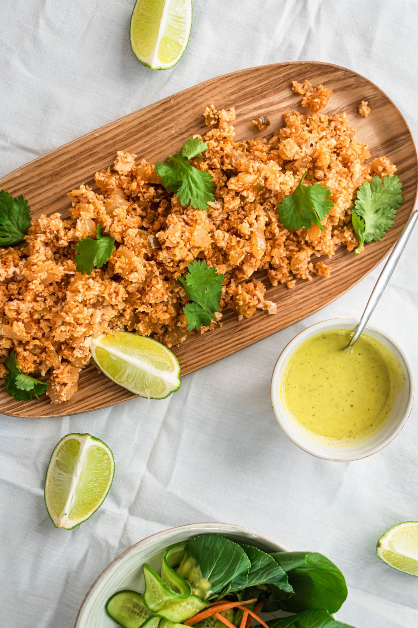 Low carb Mexican cauliflower with spice, onion, garlic, and tomato on a wooden plate with lime and cilantro.