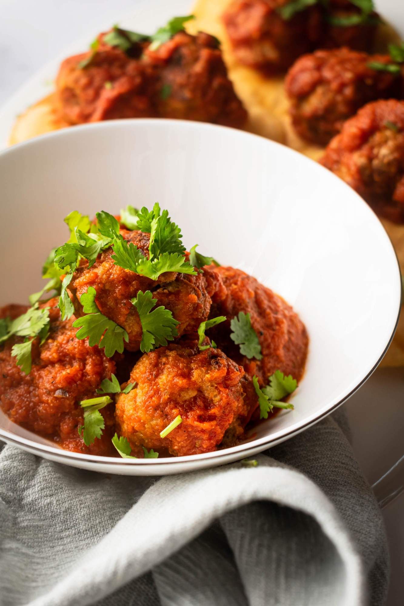 Mexican meatballs simmered in a tomato chipotle sauce in a bowl with cilantro leaves.