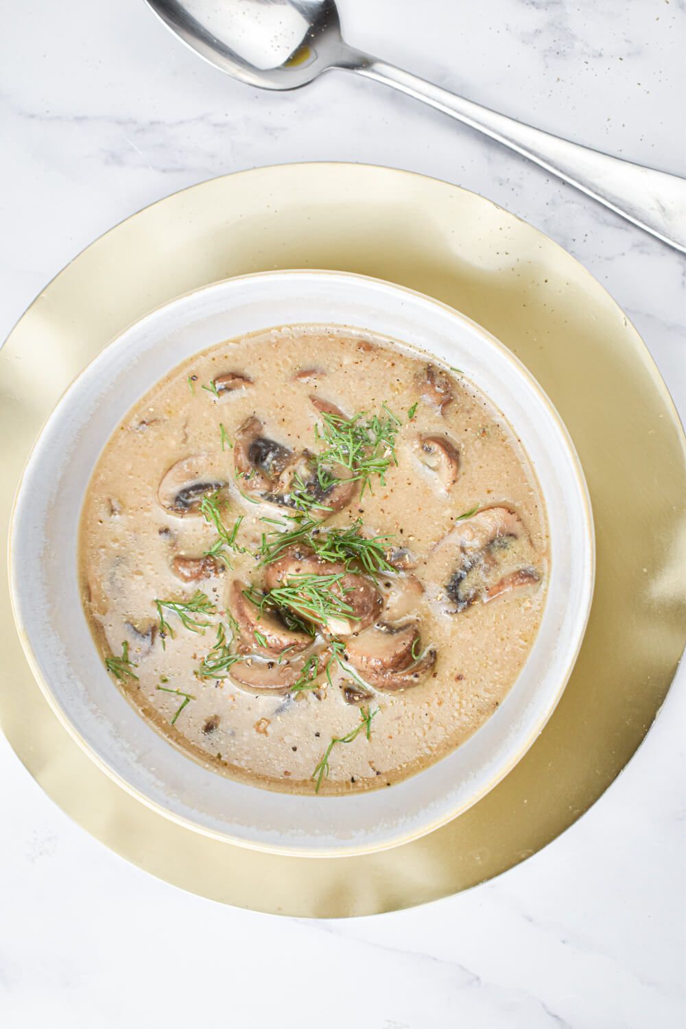 Mushroom soup with fresh mushroom, thyme, and a creamy broth in a bowl with a spoon.