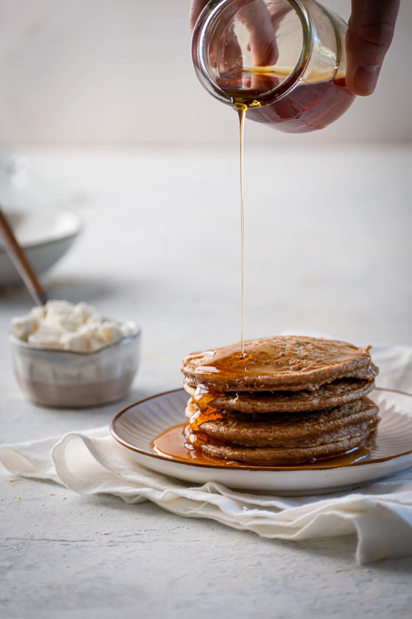 Protein pancakes with with oatmeal on a plate with maple syrup being poured on top.