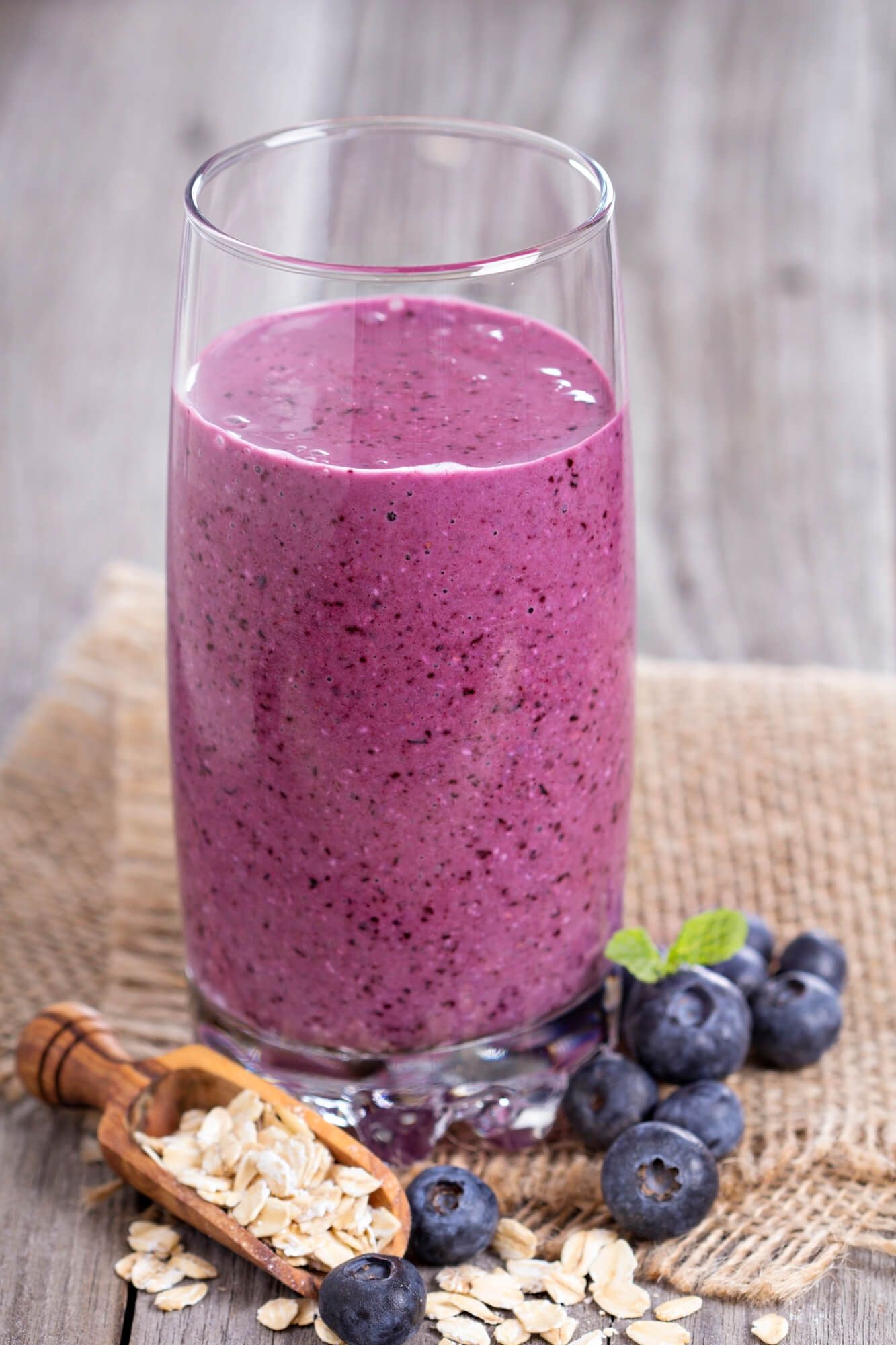 Oatmeal smoothie in a tall glass with blueberries and oats on the side.