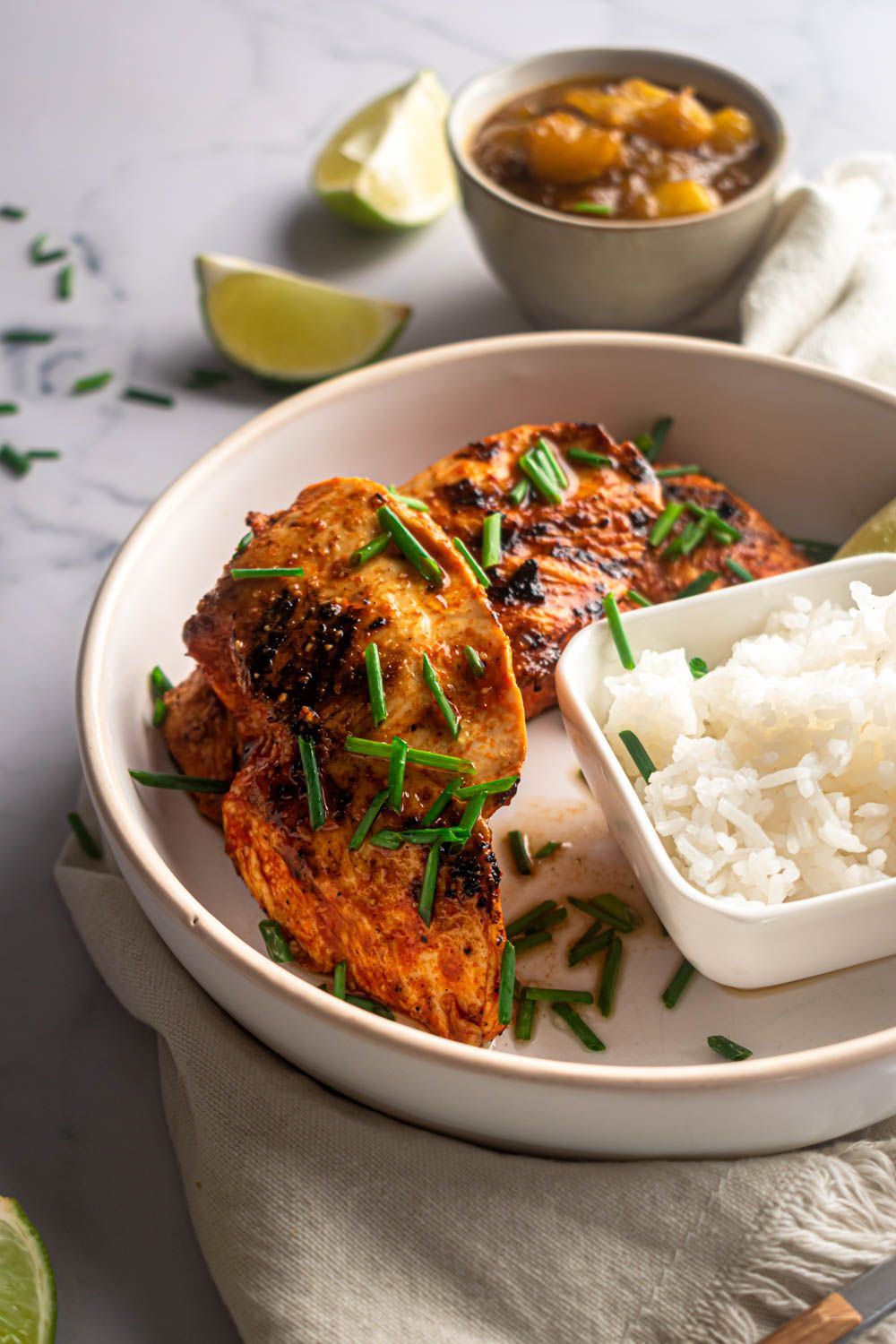 Crispy paprika lime chicken breast with sliced green onions on a plate with fresh limes and rice.