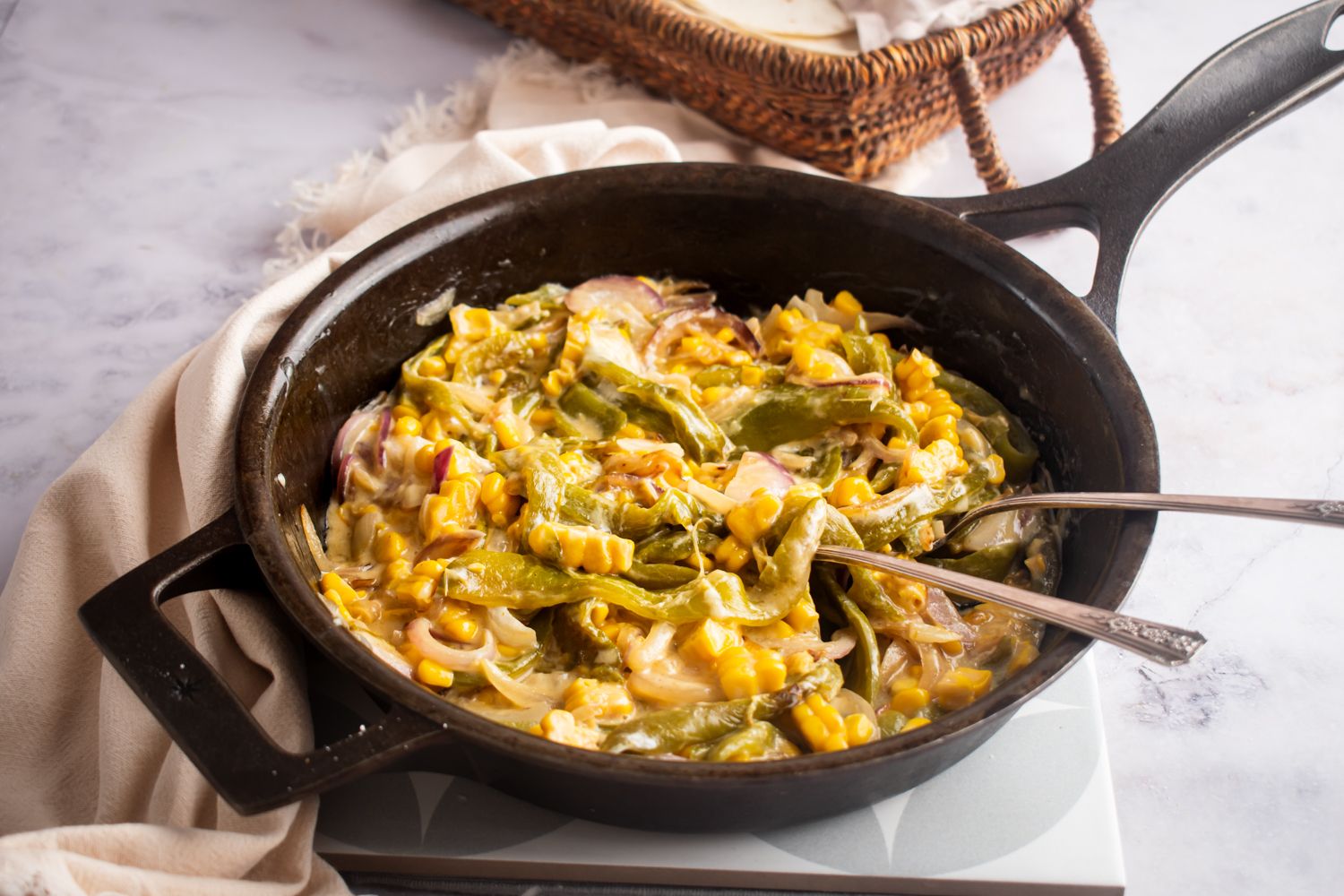 Mexican rajas con queso in a skillet with corn, poblano peppers, and red onions served with two forks.