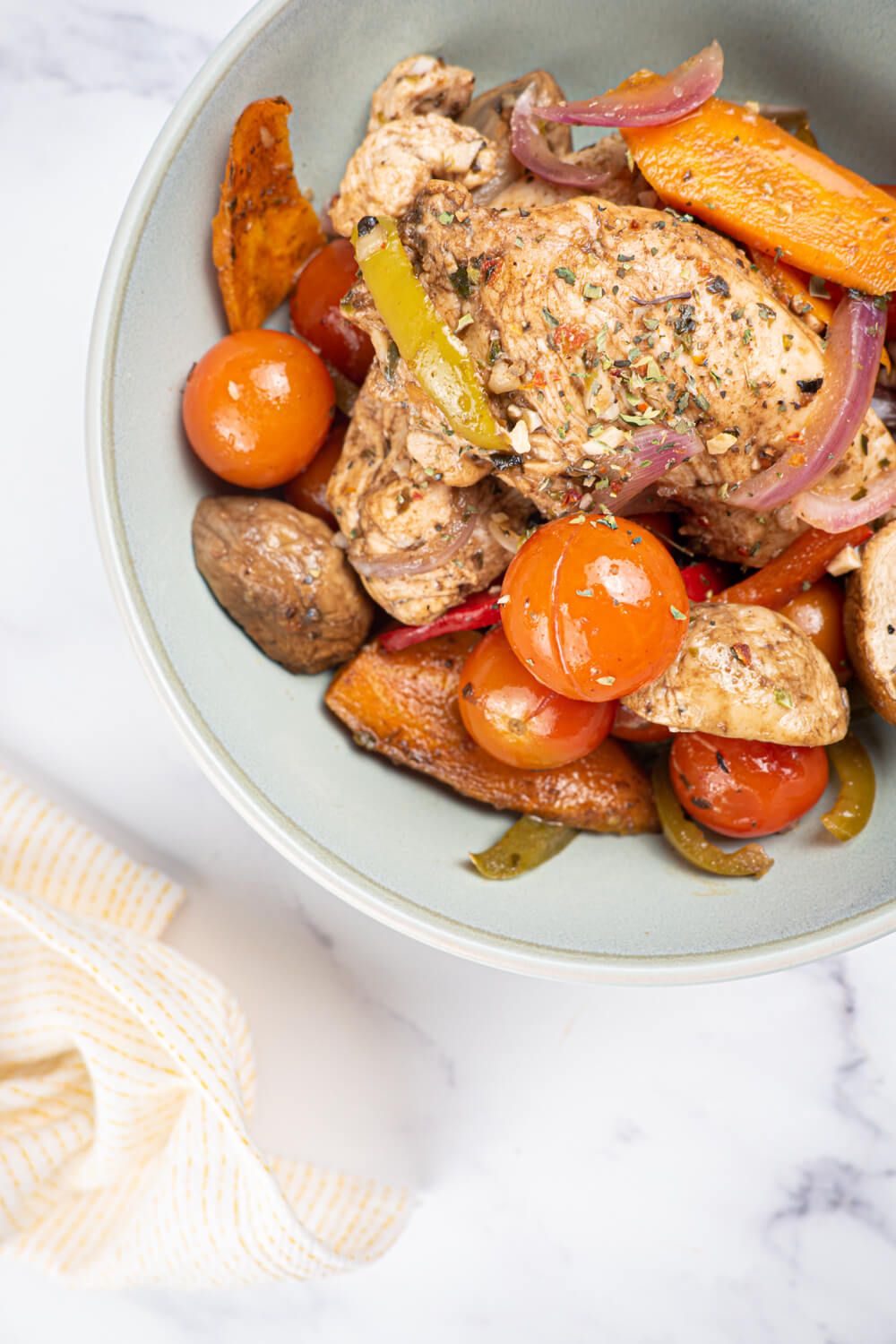 Balsamic chicken in a bowl with cherry tomatoes, mushrooms, carrots, and peppers.