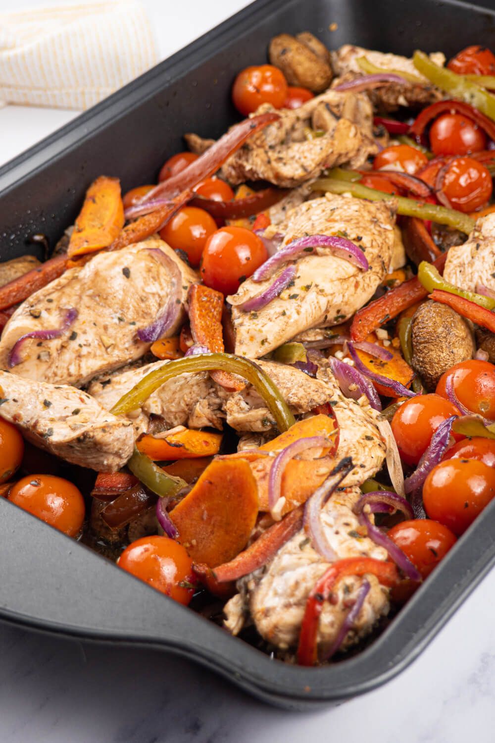 Balsamic chicken and vegetables and a sheet pan with a yellow striped napkin.