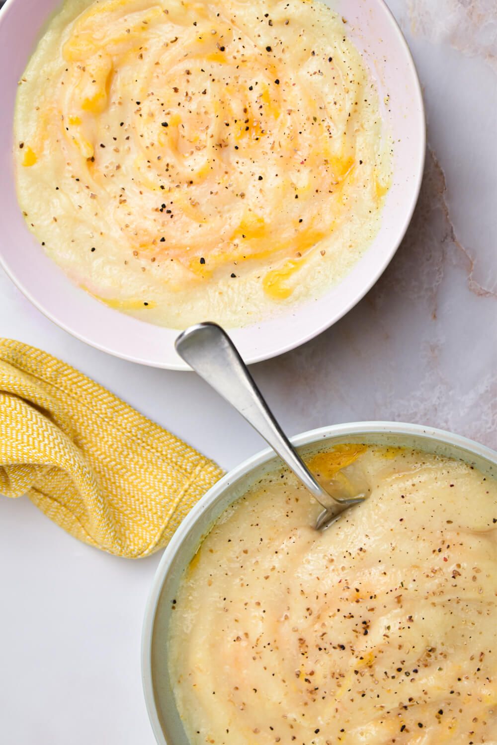 Crockpot cauliflower soup with cheddar cheese and pepper in two bowls with spoons.