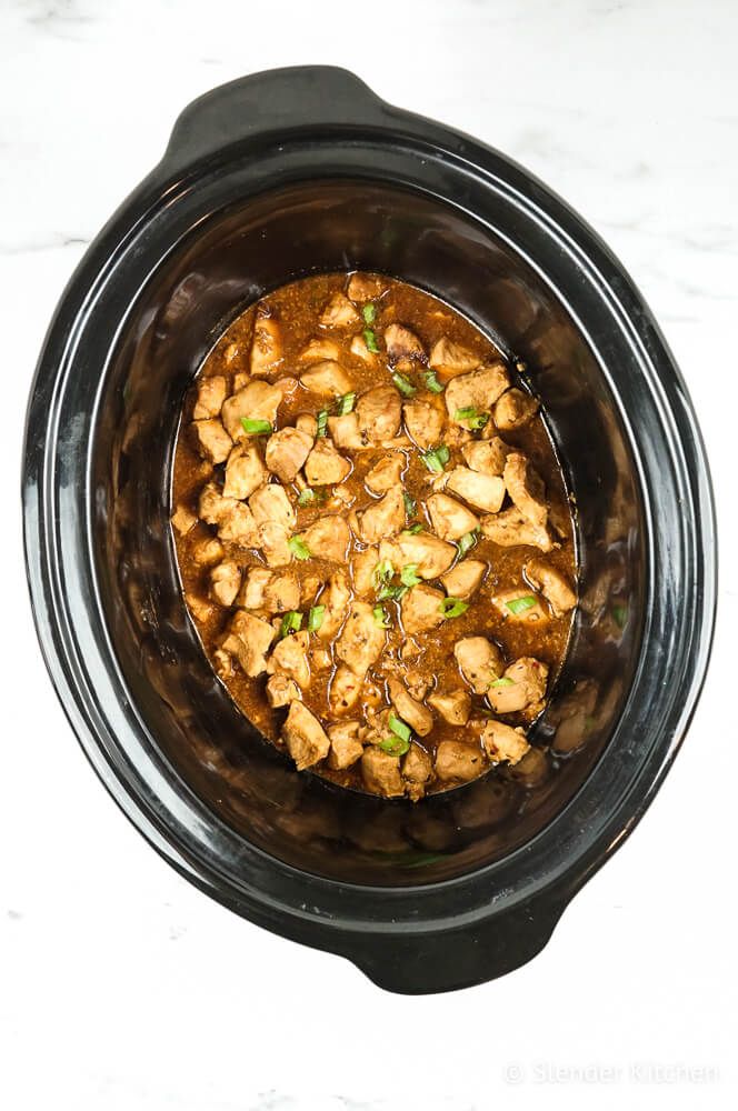 Honey garlic chicken in a slow cooker with sliced green onions and a sticky sauce.