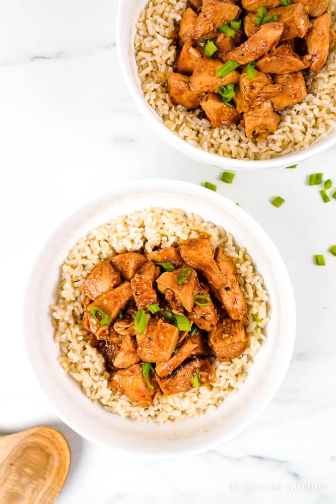 Crockpot honey garlic chicken cut into cubes with green onions and brown rice.
