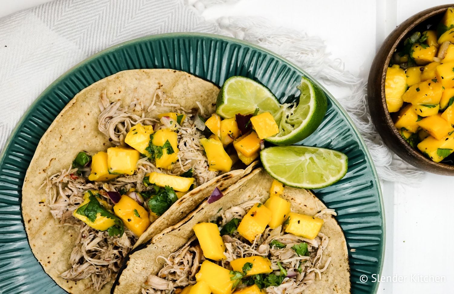 Slow cooker jerk chicken in a bowl with spices, lime juice, cilantro, and mango salsa.