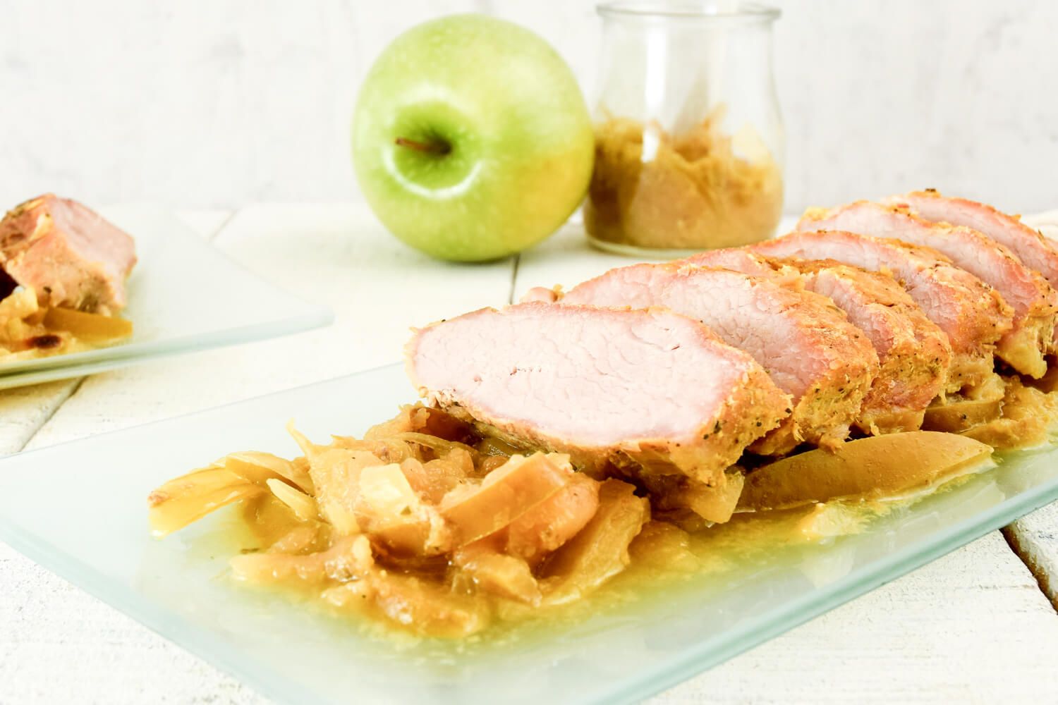 Slow cooker pork and apples on a glass plate with cooked apples and onions.