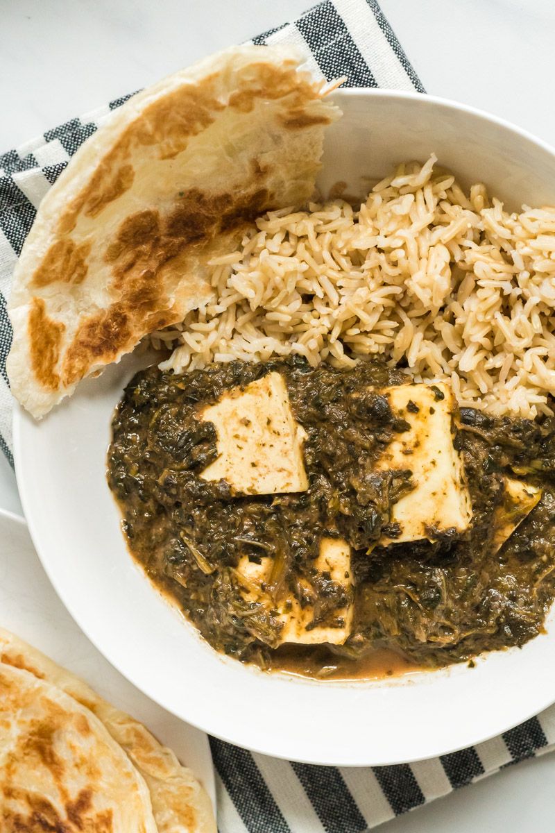 Indian saag paneer with spinach, garam masala, and paneer cheese in a bowl with steamed brown rice and Indian naan bread.