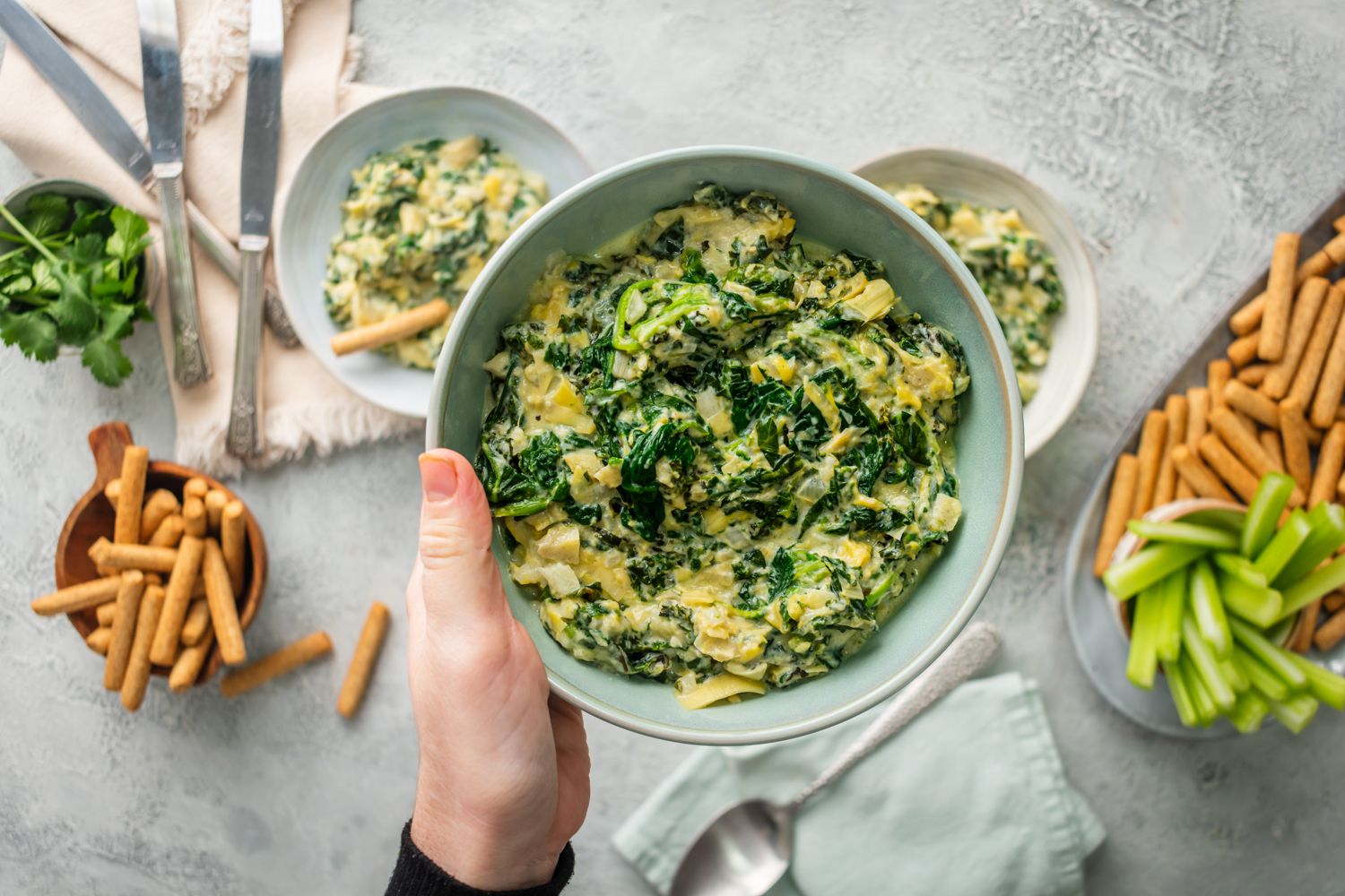 Spinach and artichoke dip with kale, Greek yogurt, and cheese in a bowl being held up by a hand.