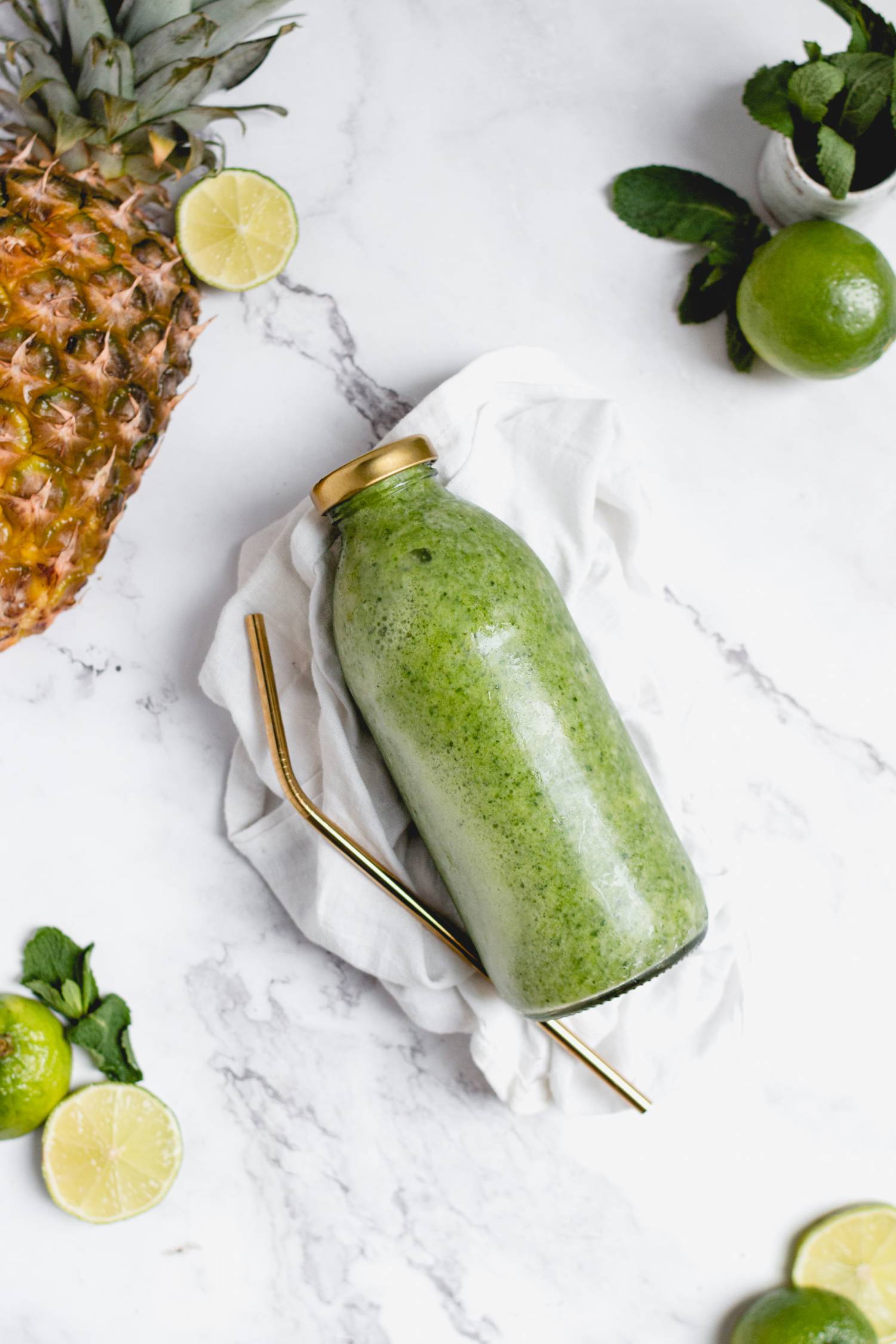 Mint fruit smoothie in a glass jar with pineapple, lime, and mint on the side.