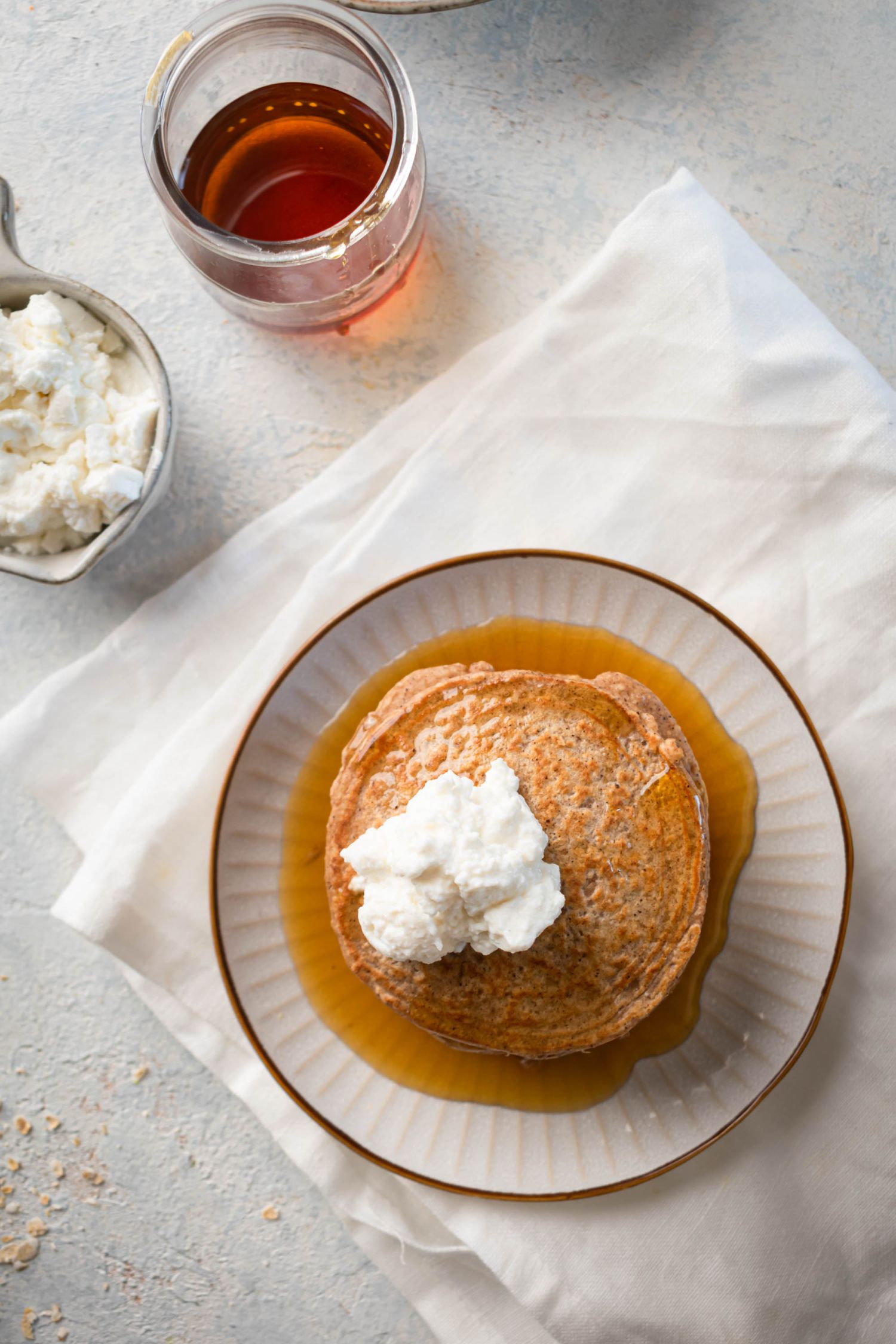 Stack of protein oatmeal pancakes served with fresh whipped cream and syrup.