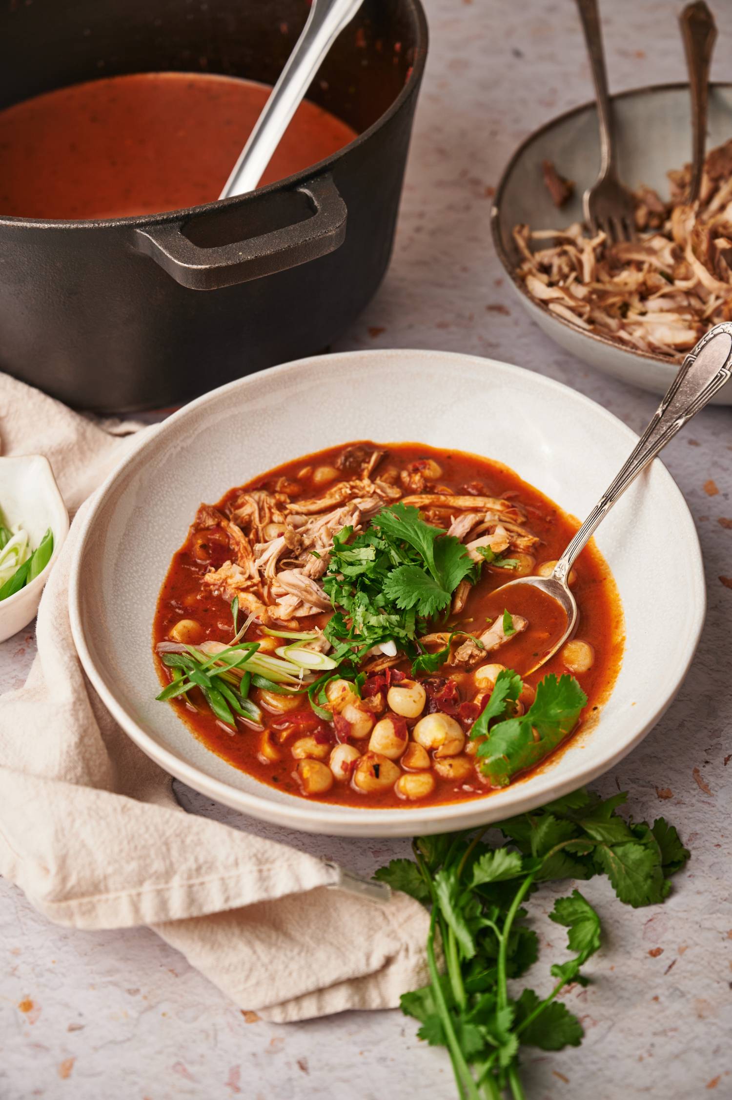 Red pozole with chicken and hominy in a bowl served with cilantro and onions.