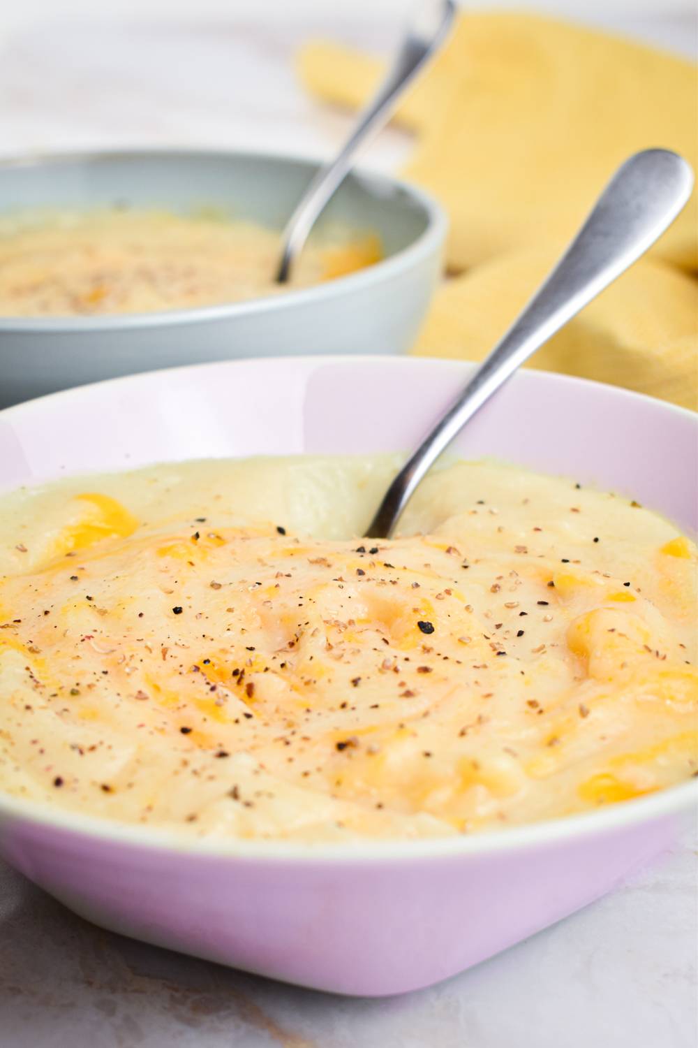 Crockpot cauliflower soup with cheddar cheese, pepper, and salt  in a bowl with a spoon.