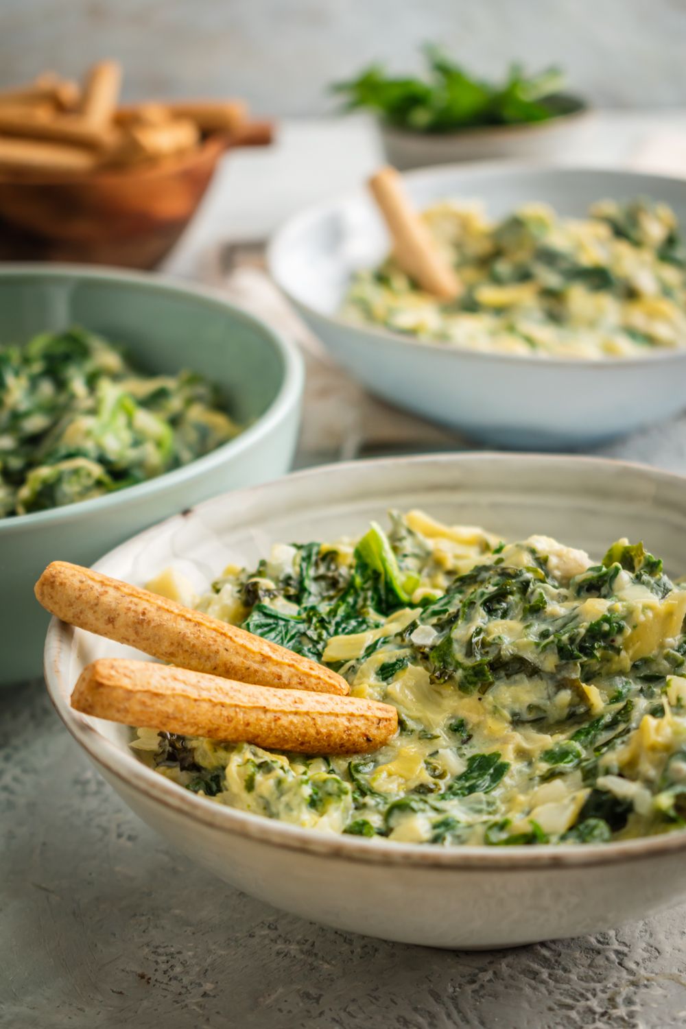 Artichoke and spinach dip with kale in a bowl with breadsticks.