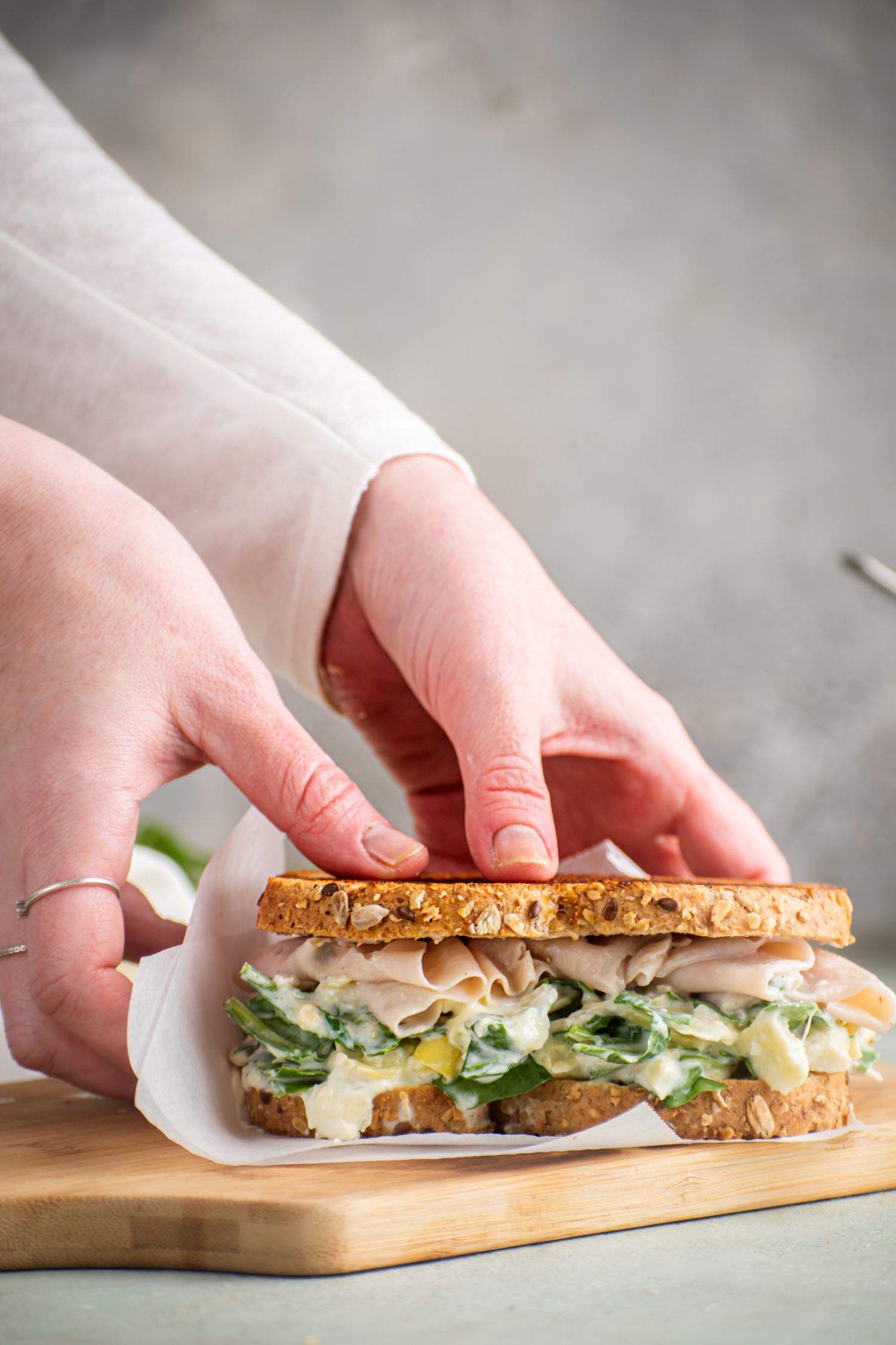 Spinach grilled cheese with artichoke, cream cheese, and mozzarella on grilled bread on a cutting board.