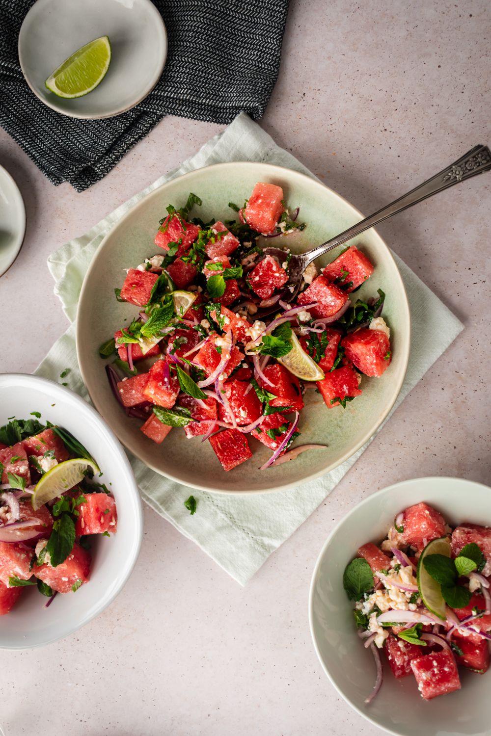 Fresh cubed watermelon tossed with feta cheese, thinly sliced red onions, and fresh mint in bowl with a spoon.