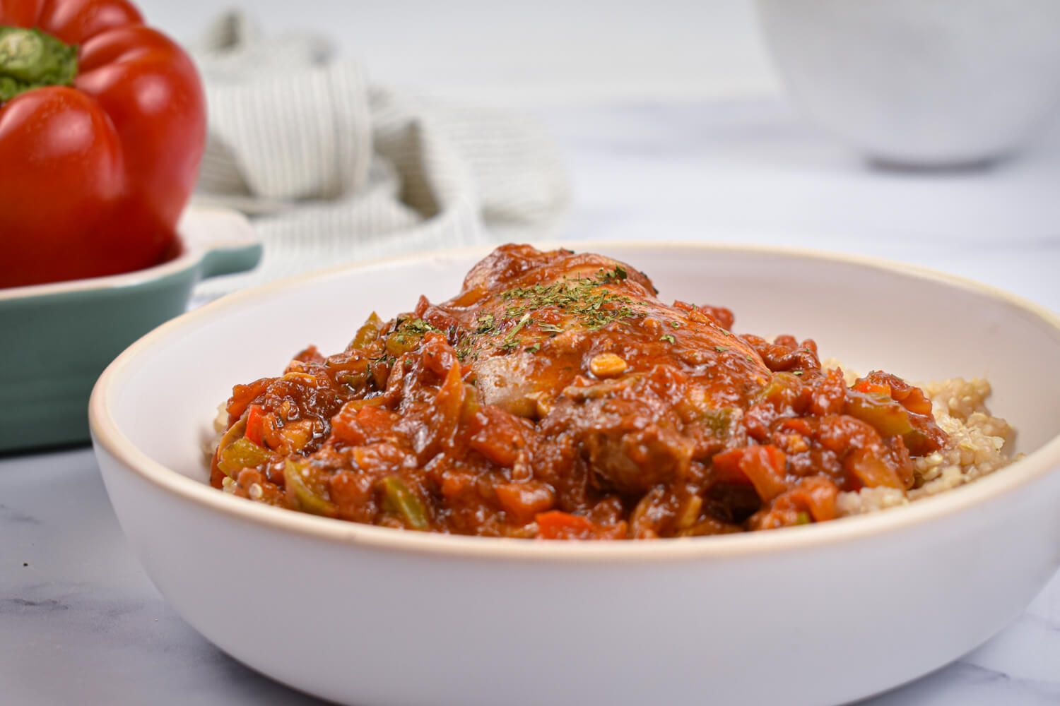 Slow cooker chicken cacciatore in a bowl with tomato sauce, chicken, mushrooms, and peppers over quinoa.