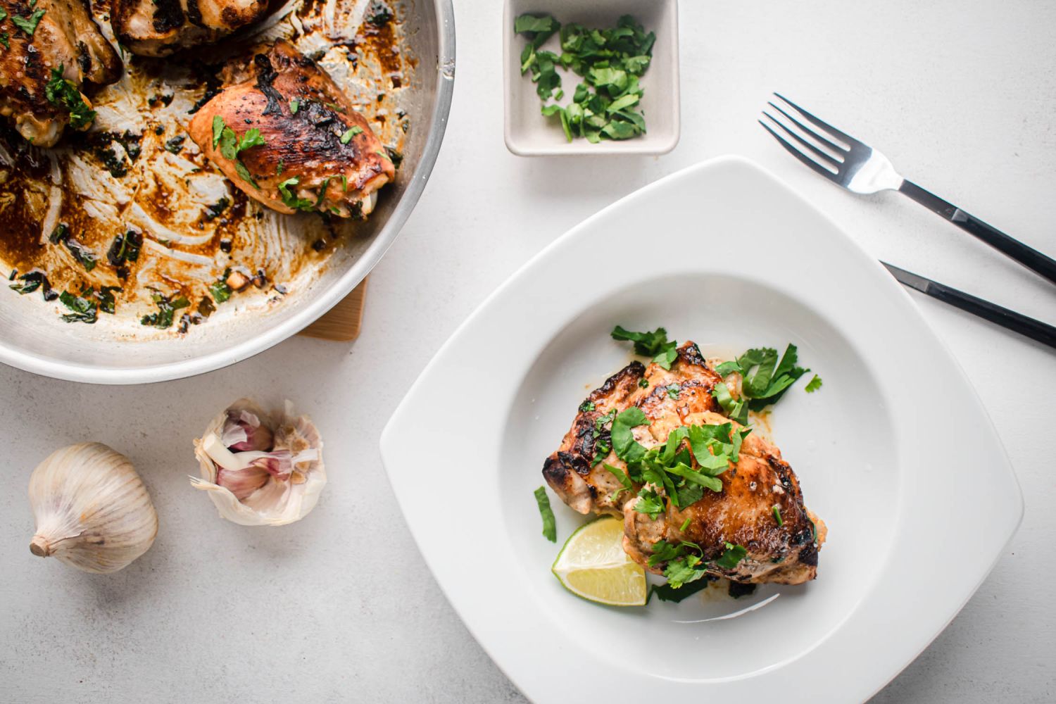 Cilantro lime chicken thighs on a plate with fresh cilantro on top and lime wedges on the side.