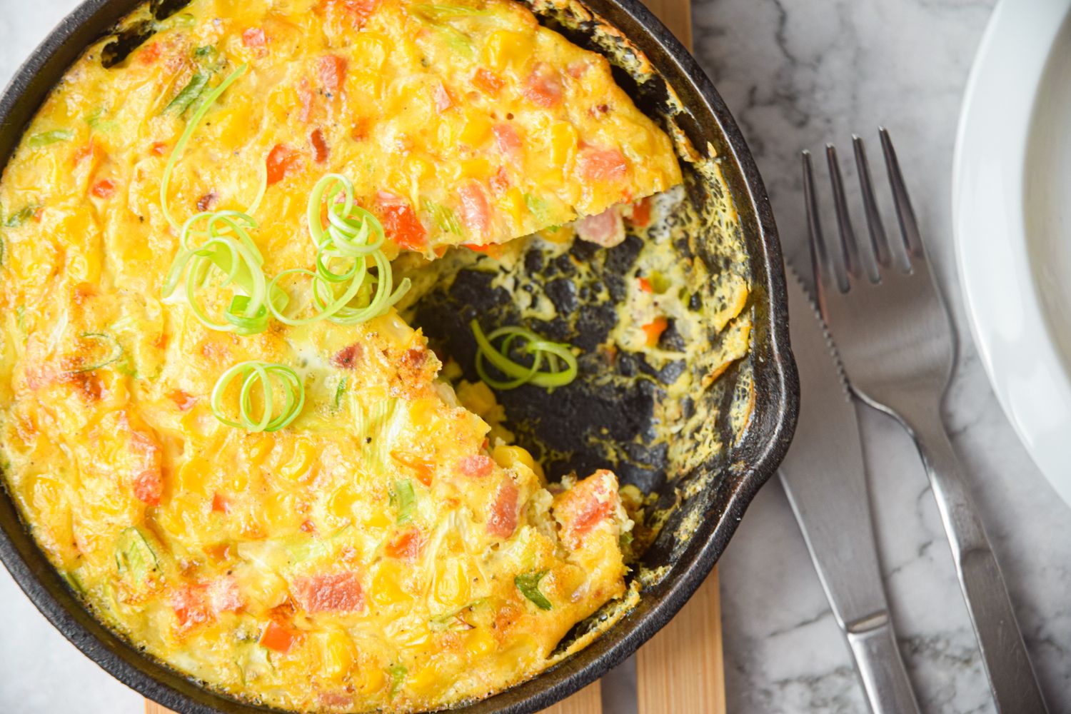 Crustless corn and bacon pie in a skillet with green onions, crispy bacon, fresh corn, and eggs.