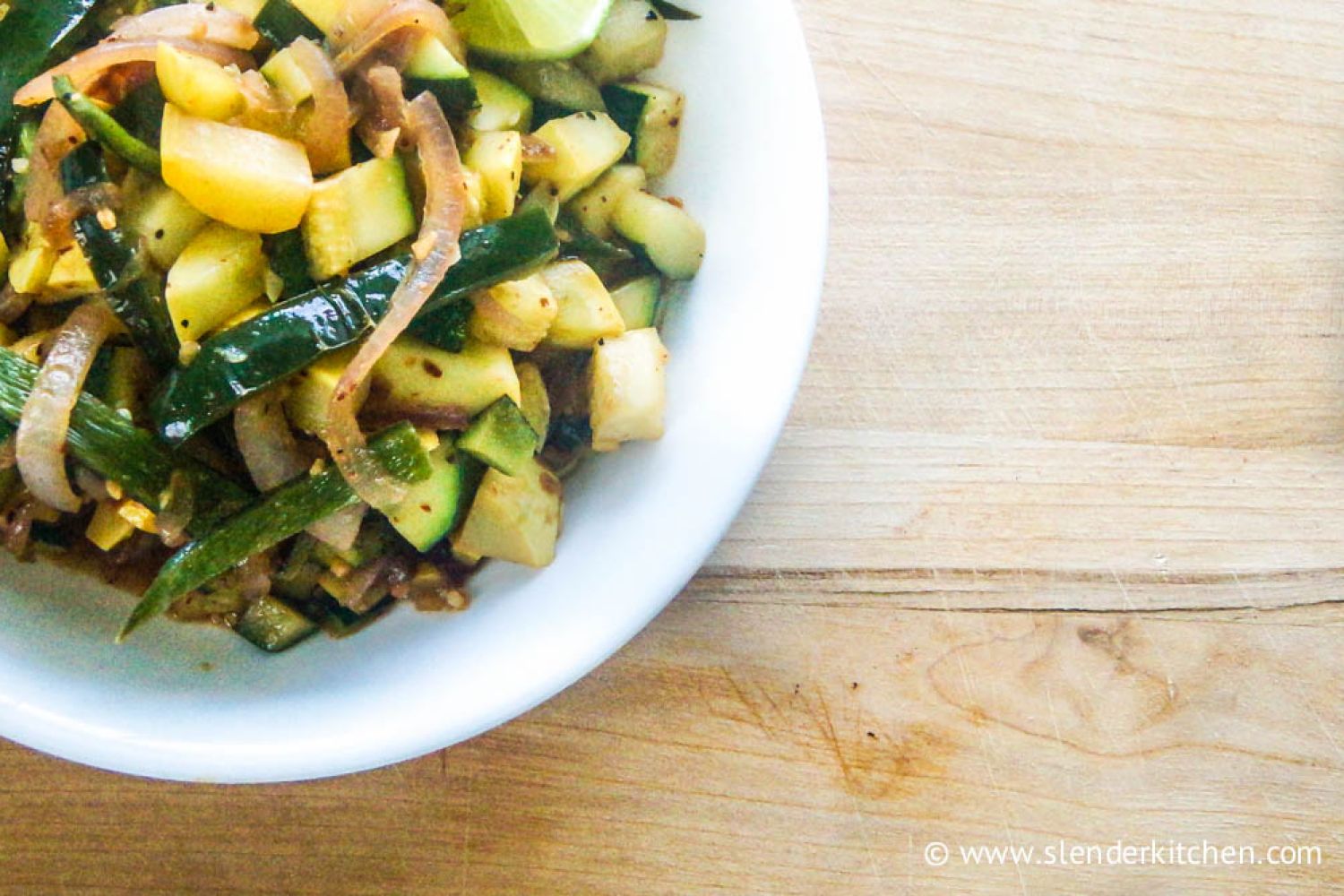 Sauteed zucchini with poblano peppers and red onions on a white plate.