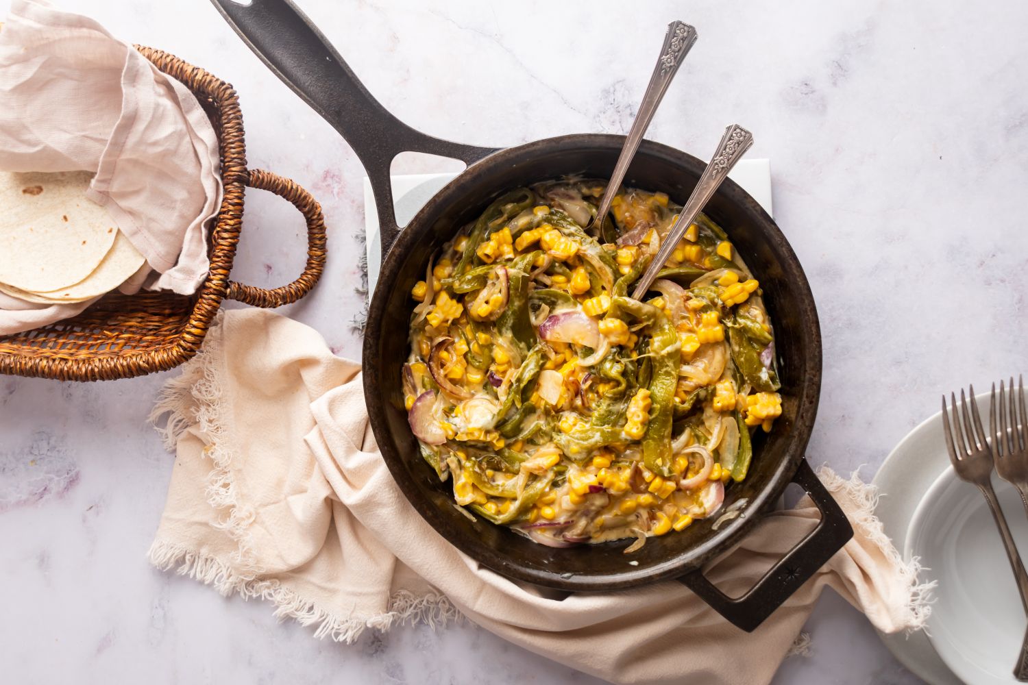 Rajas con queso in a skillet with poblano peppers, red onion, corn, and cheese sauce. with flour tortillas on the side.