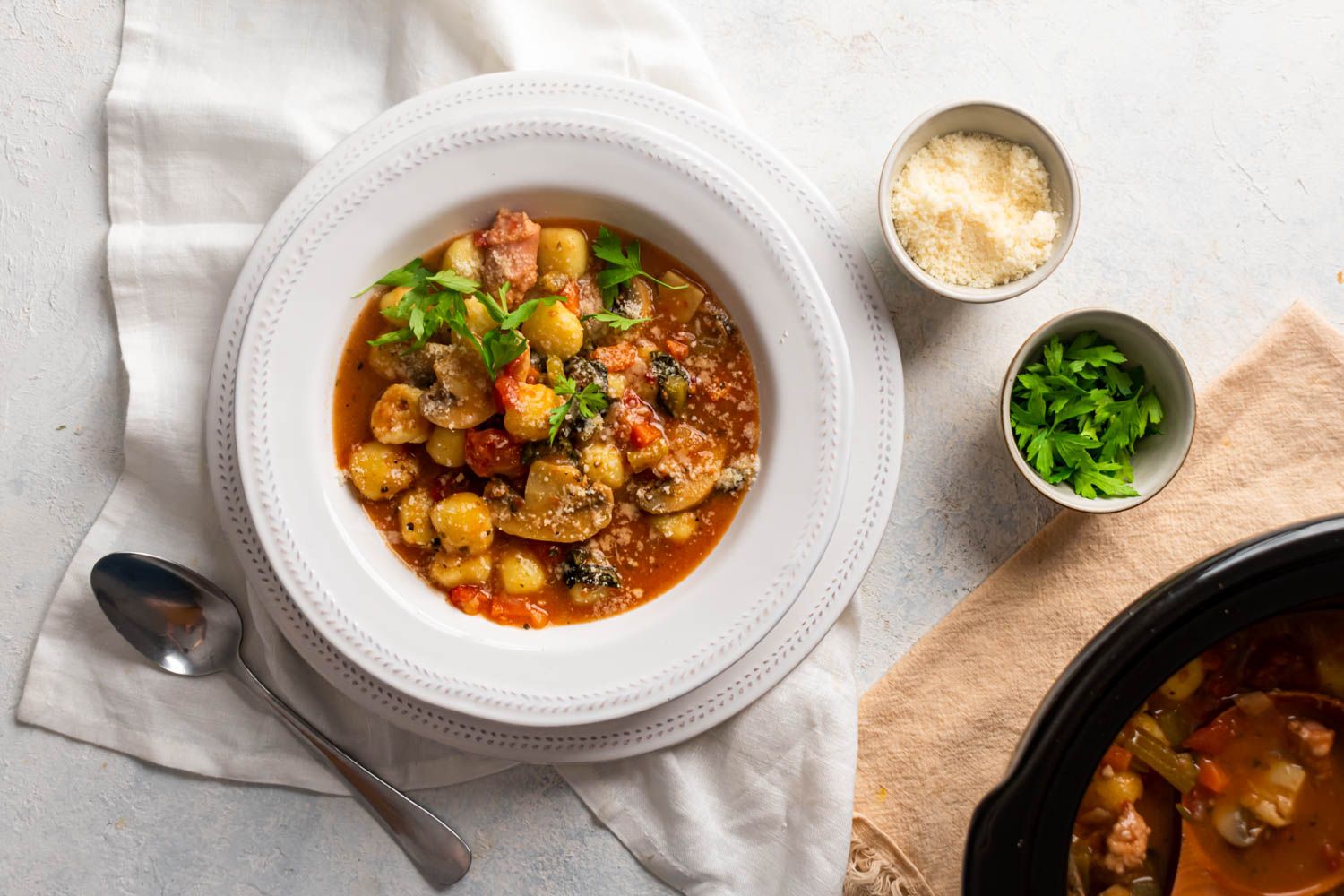 Slow cooker sausage and gnocchi soup with mushrooms, spinach, Parmesan cheese, and a rich tomato broth in a bowl.