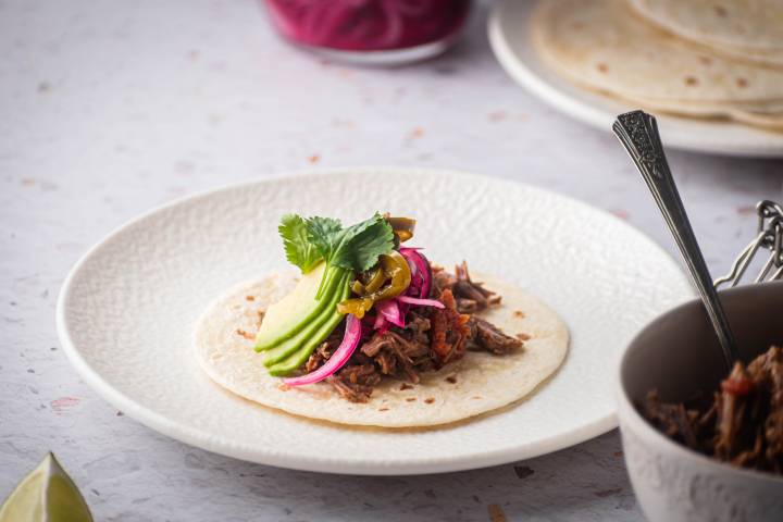 Shredded beef being served in a flour tortilla with avocado, pickled red onions, and jalapeno.