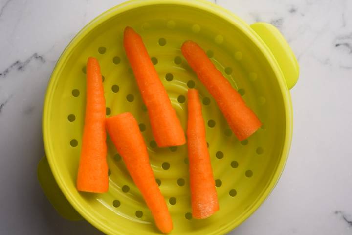 Steamed carrots on a green steamer basket.