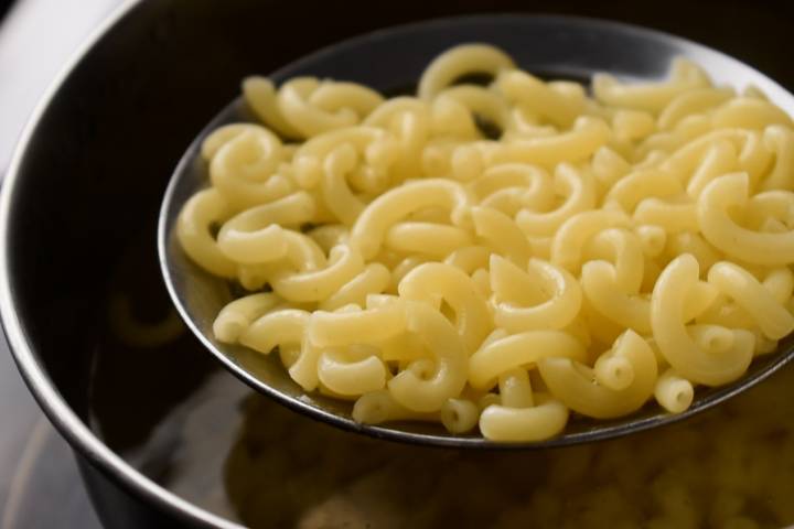 Elbow macaroni cooking in a pot and a slotted spoon.