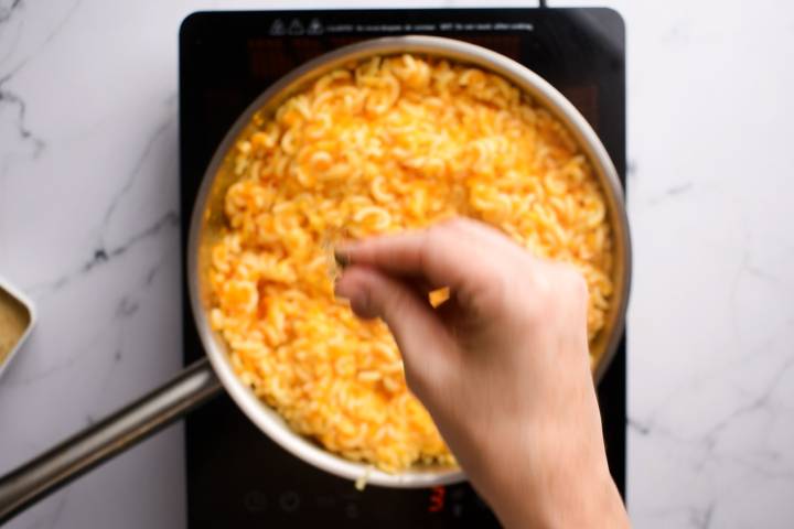 Carrot puree and cheese being added to pasta in a skillet.