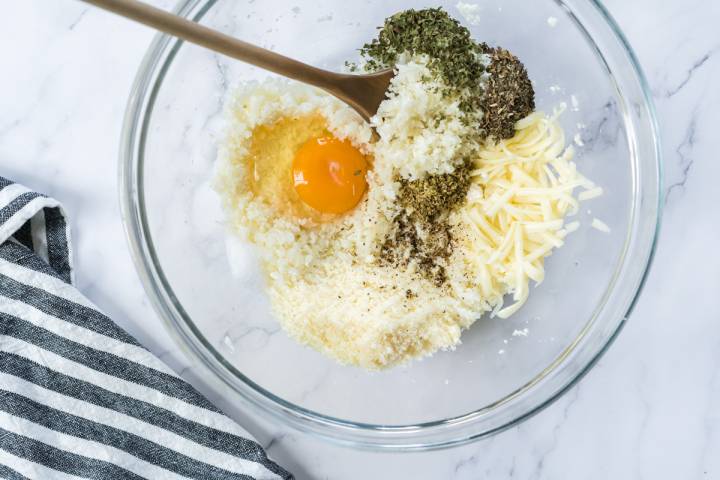 Cauliflower rice, eggs, herbs, and cheese in a glass bowl.