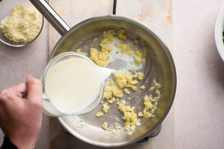 Garlic, onion, and butter cooking in a skillet with milk being poured in.