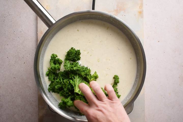 Kale being added to a cheesy cream sauce.