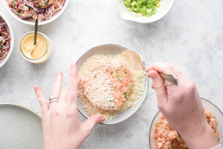 Easy Salmon Burgers Salmon burger patties being coated with breadcrumbs on a shallow plate.