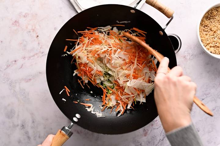 Shredded cabbage, carrots, green onions, ginger, and garlic cooking in a wok.