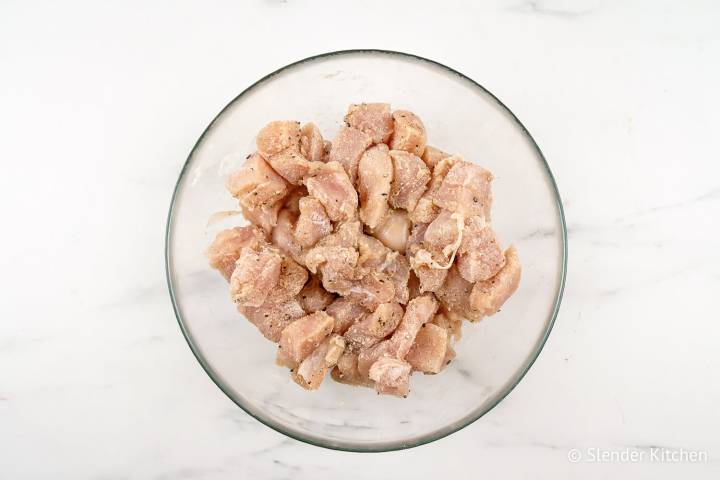 Chicken breast tossed with cornstarch, salt, and pepper in a bowl.