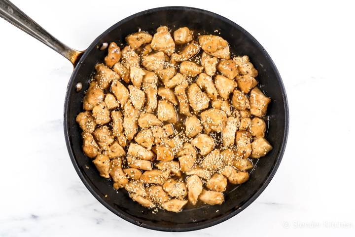 Healthy sesame chicken in a thick sesame sauce in a skillet with sesame seeds.