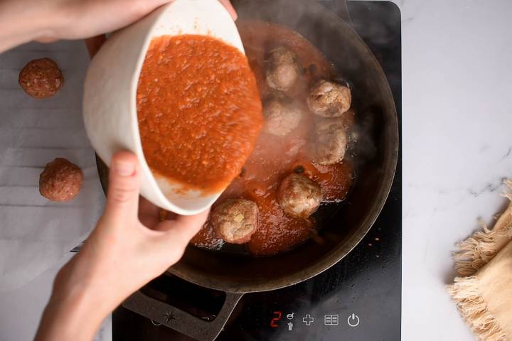 Chipotle sauce being added to meatballs in a skillet to simmer.